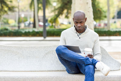 Young man using digital tablet while sitting on bench