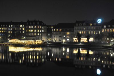 Illuminated buildings by river against sky in city at night