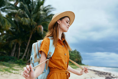 Young woman looking away while standing against tree