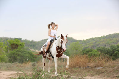 Young woman riding horse on field against sky