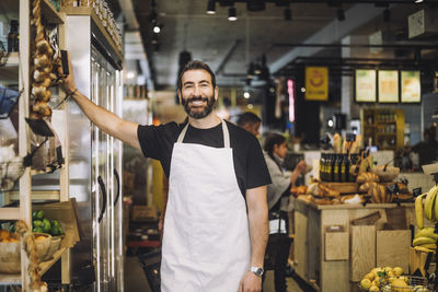 Portrait of smiling male retail clerk standing by rack at organic grocery store