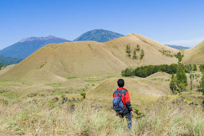 Rear view of man walking on mountain against clear sky