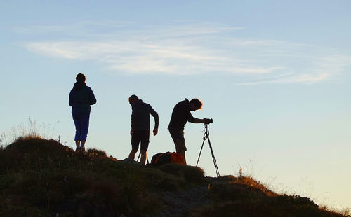 Silhouette friends standing on land against sky during sunset