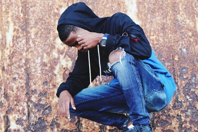 Young man crouching and looking down against metal wall