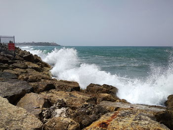 Scenic view of sea waves splashing on rocks against sky