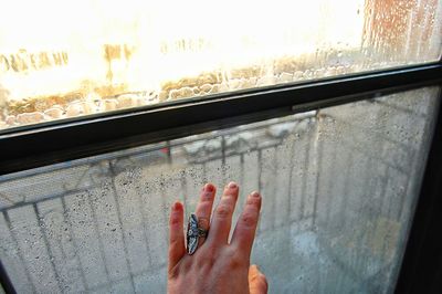 Cropped hand of woman touching wet window during rainy season