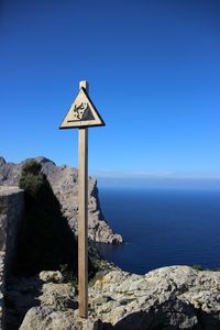 Close-up of road sign by sea against clear blue sky