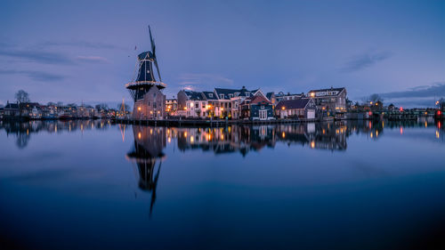 Illuminated buildings by lake against sky at night