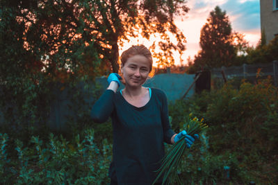 Portrait of smiling woman holding plants against trees