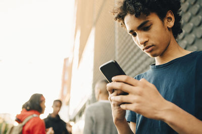 Teenage boy using mobile phone while friends standing in background on city street