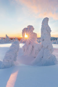 Snow covered land against sky during sunset