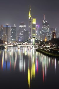 Illuminated buildings by river against sky at night