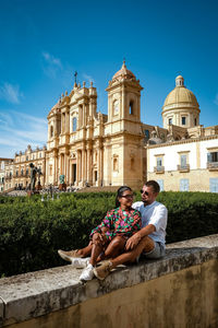 Couple sitting against built structure