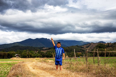 Portrait of boy pointing while standing on grass against sky