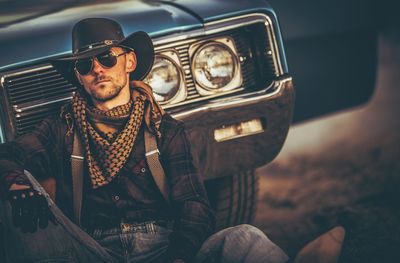 Portrait of man sitting against car on field