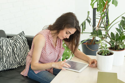 Young woman using phone while sitting on table at home