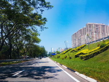 Road by trees in city against sky