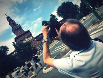 Portrait of man photographing on city against sky