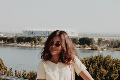Portrait of beautiful woman standing by lake against clear sky