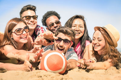 Young friends enjoying rugby at beach against sky