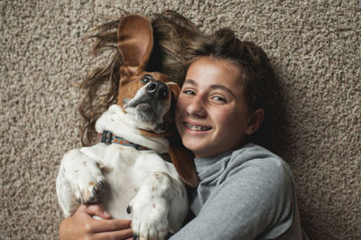 Tween girl posing with her basset hound dog while laying on the carpet