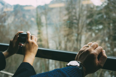 Cropped hands of people on railing by glass window