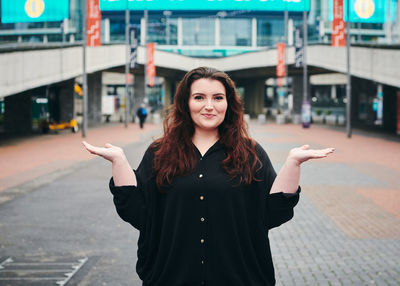 Portrait of young woman gesturing while standing on footpath in city