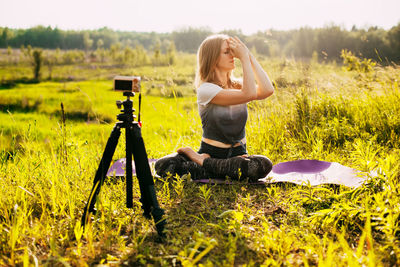 A young girl is doing yoga, sitting in the lotus position in nature and recording a video lesson