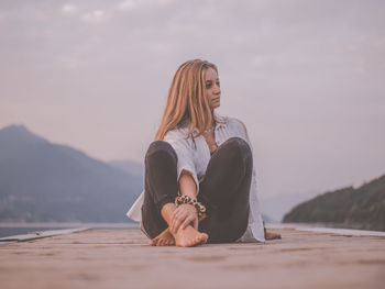 Woman sitting on mountain against sky