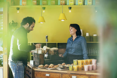 Happy waitress looking at male customer adding sugar in coffee