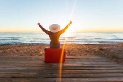 Man with arms raised on beach against sky during sunset