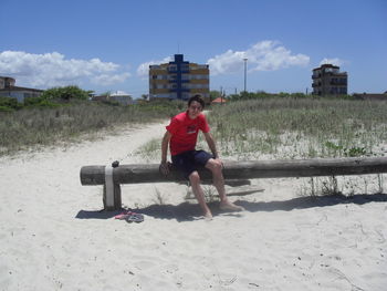 Full length of woman sitting at beach against sky