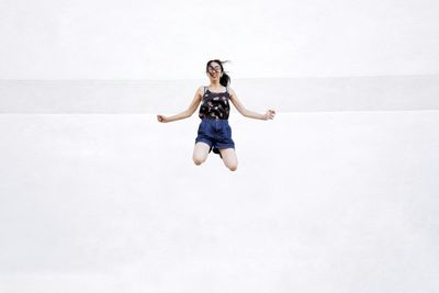 Full length of young woman jumping against wall