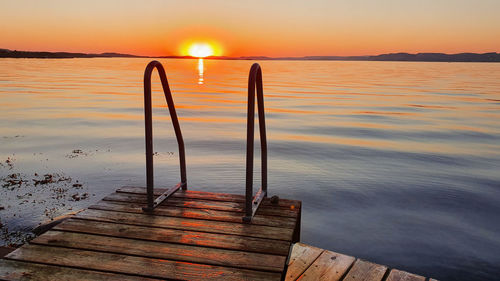 Wooden post on pier over sea against sky during sunset