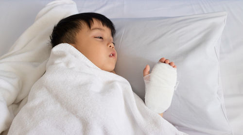 Close-up of boy with bandage on hand lying at home