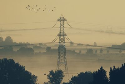 Silhouette trees and electricity pylon against sky during sunset