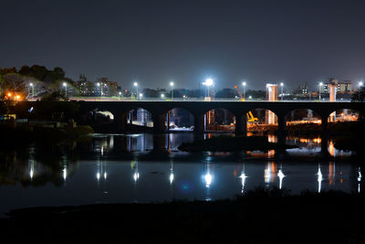 Illuminated bridge over river in city at night