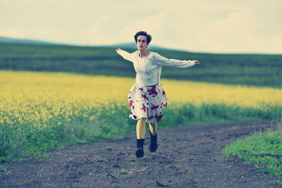 Full length portrait of young woman standing on field