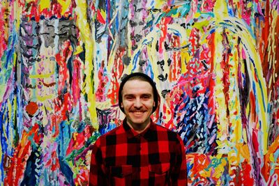 Portrait of young man smiling by colorful graffiti wall