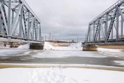 Bridge over frozen river against sky during winter