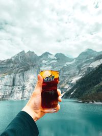 Person holding ice cream by lake against mountains