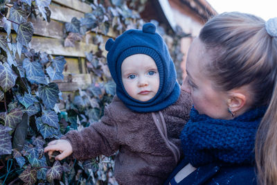 Portrait of cute baby boy. woman holding baby in her hands against ivy-covered wooden wall. 