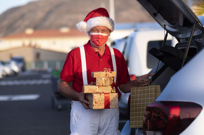 Portrait of man holding hat while standing by car