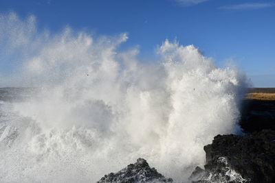 Sea waves splashing on rocks against sky