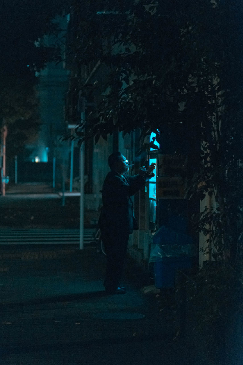 REAR VIEW OF MAN WALKING ON FOOTPATH AT NIGHT