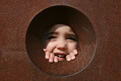 Close-up portrait of smiling girl peeking from hole