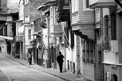 Rear view of man walking on street amidst buildings in city