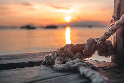 Close-up of rope tied up to pier against sea during sunset