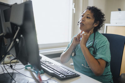 Female doctor giving advice through video call while sitting at desk in hospital