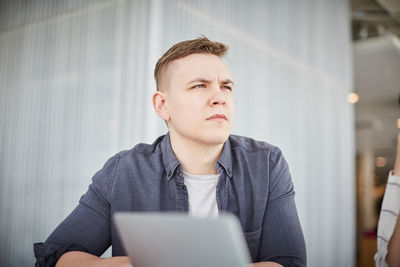 Thoughtful young student looking away while sitting at university cafeteria